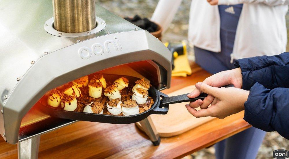 someone putting a smores dessert into a pizza oven 